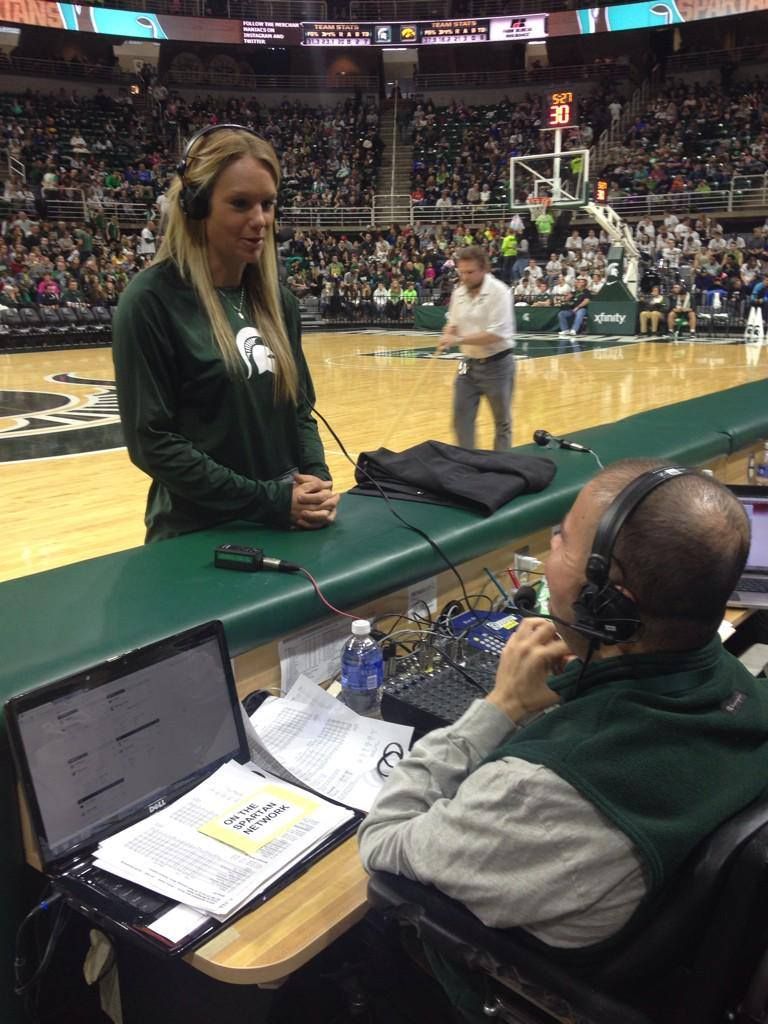 Arena announcer speaking courtside during a basketball game, with a headset operator at a console.