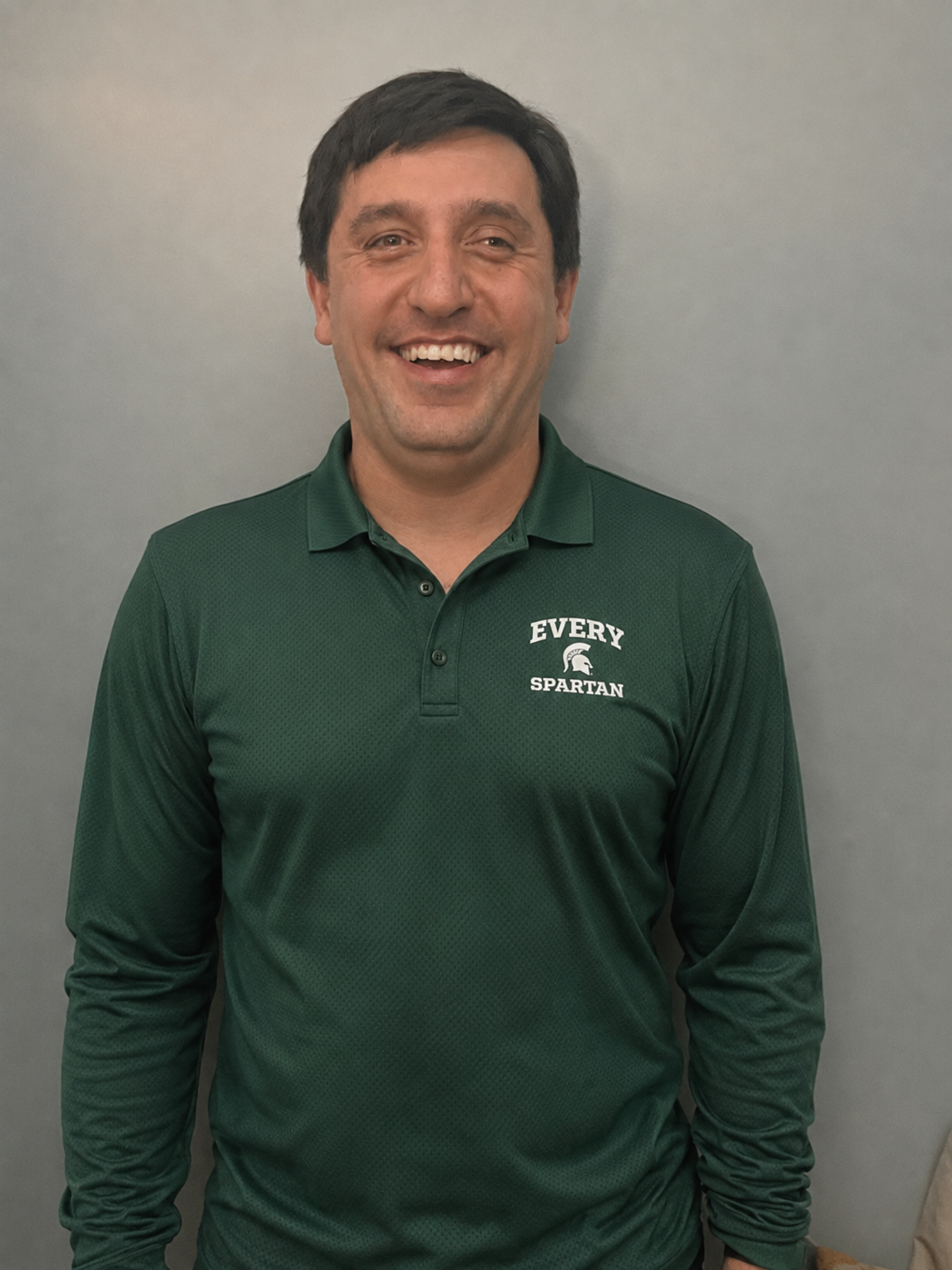 Smiling man in green long-sleeve polo standing against a plain gray background