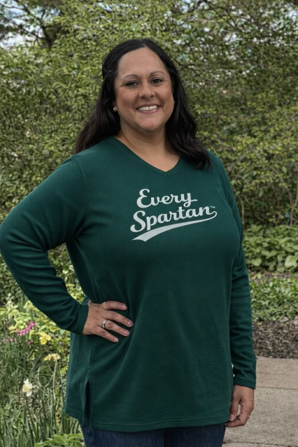 A smiling person wears a green long-sleeved shirt that says 