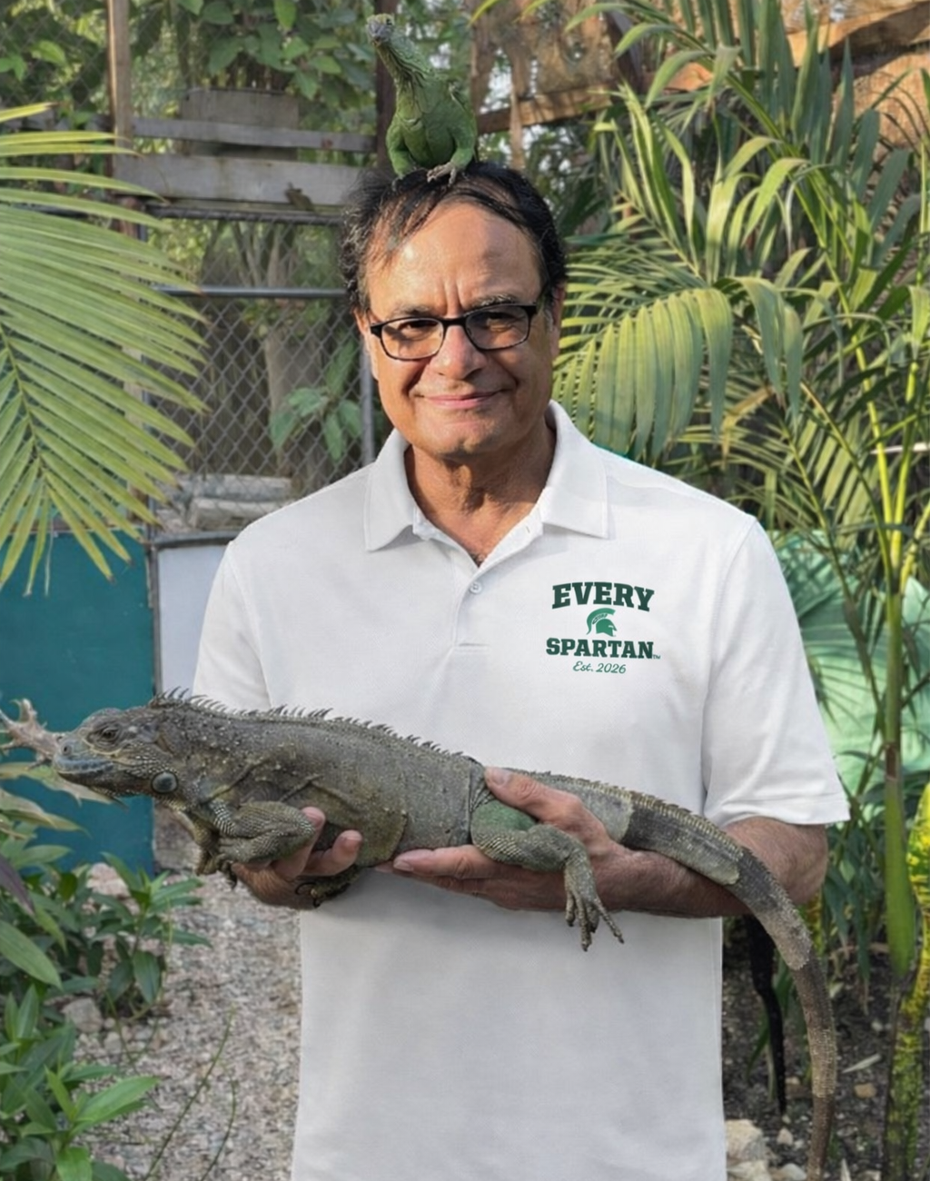 Man holding a large green iguana; another iguana on his head, tropical setting.