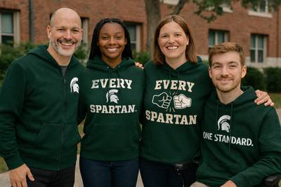 Four people in green “EVERY SPARTAN” sweatshirts standing outdoors in front of a building