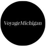 Black circular logo with white text reading “VoyageMichigan”