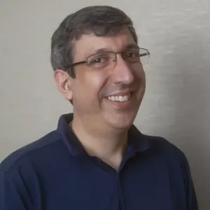 A man wearing glasses and a blue shirt is smiling