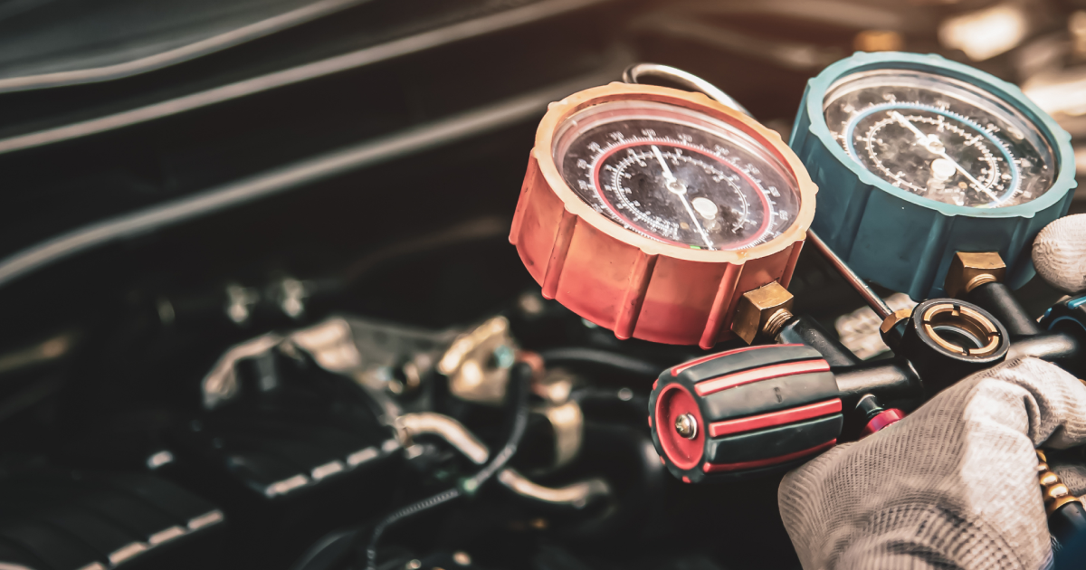 A person checks a car's AC system with gauges. Gauges are red and blue. Engine bay is visible.