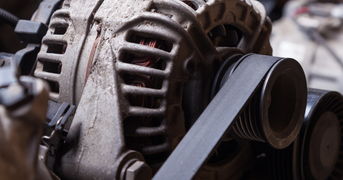 Alternator with belt connected to an engine. Gray, dusty, close-up shot.