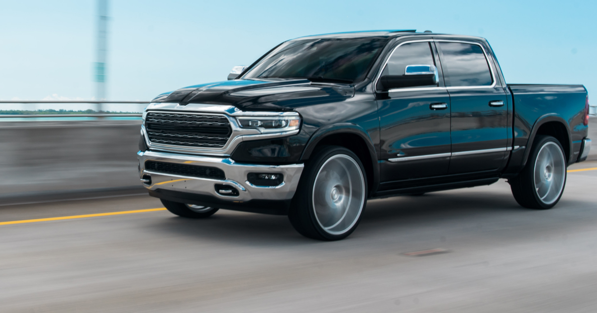 Black Ram truck with chrome accents driving on a bridge, blue sky background.