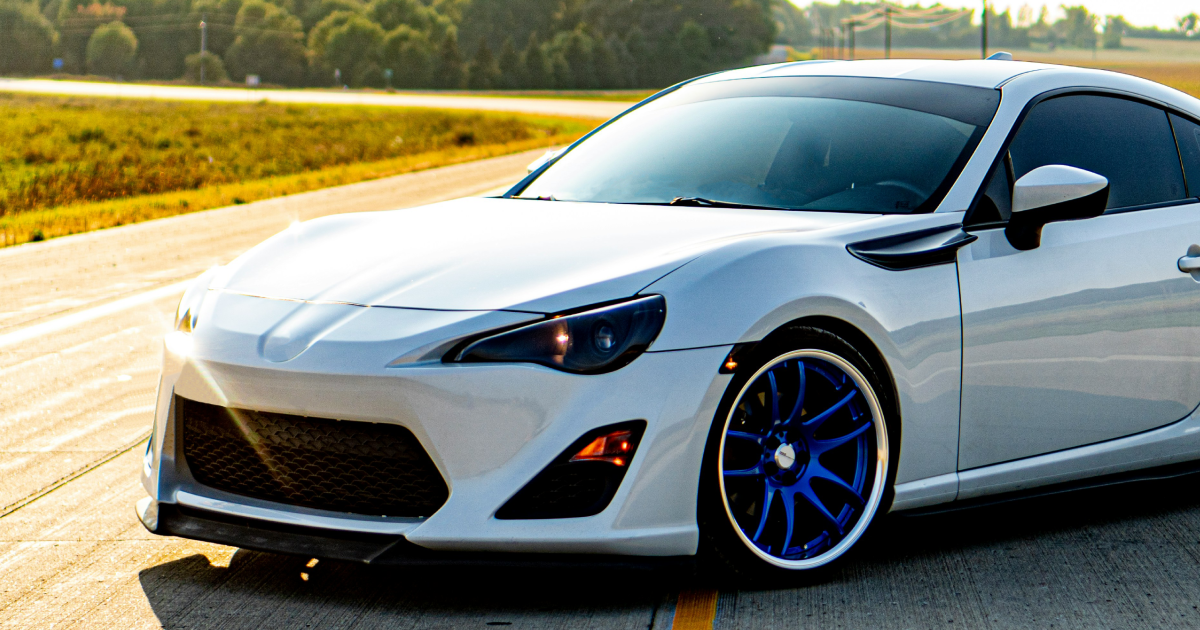 White sports car with blue rims driving on a road.