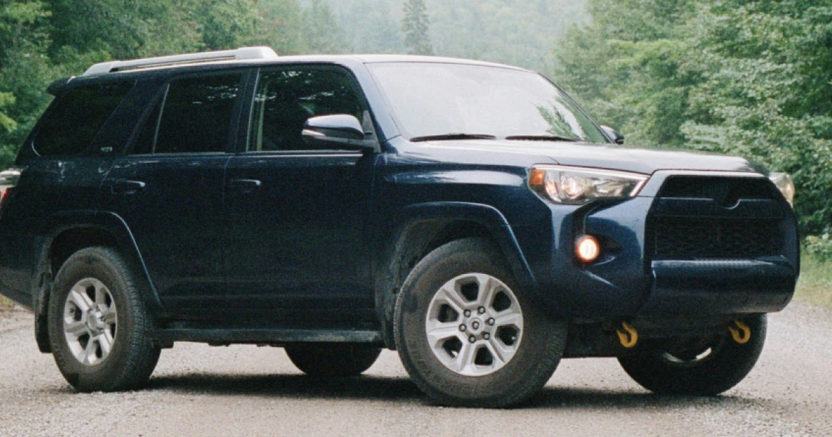 Dark blue Toyota 4Runner SUV parked on a dirt road, with trees in the background.