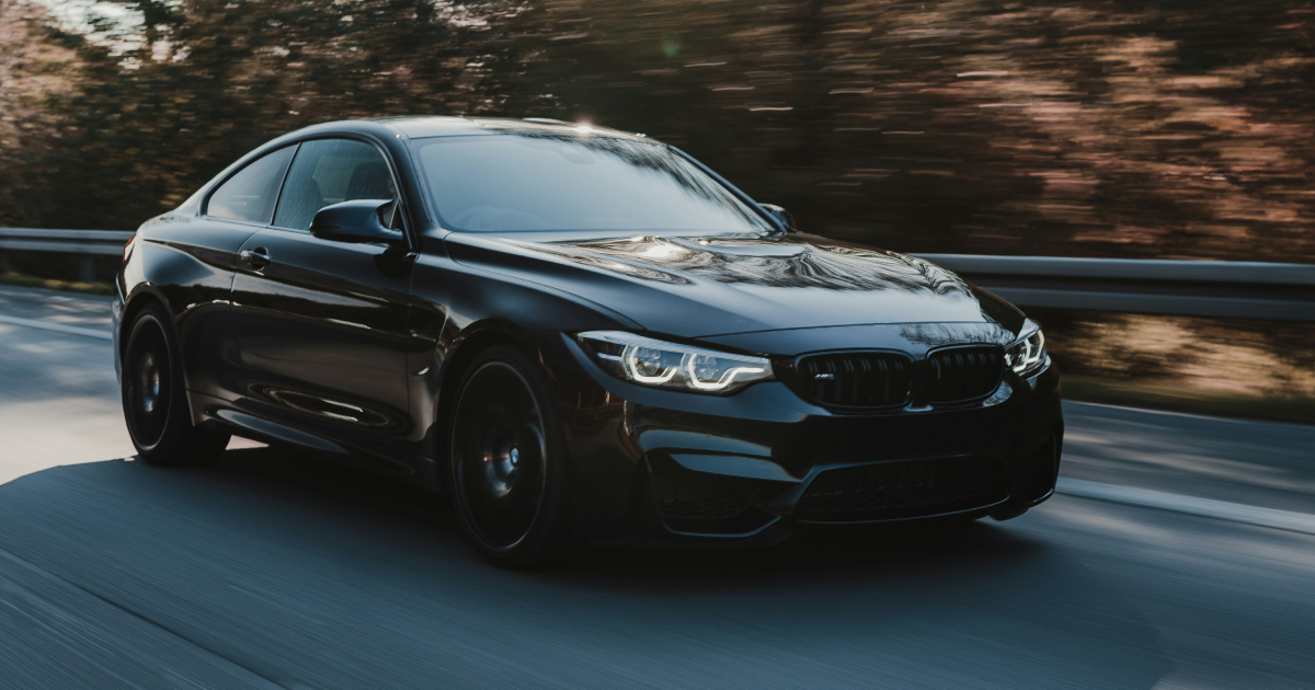 Black BMW coupe driving on a road, trees blurred in the background.