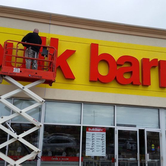 A man on a scissor lift installing a sign for k barn
