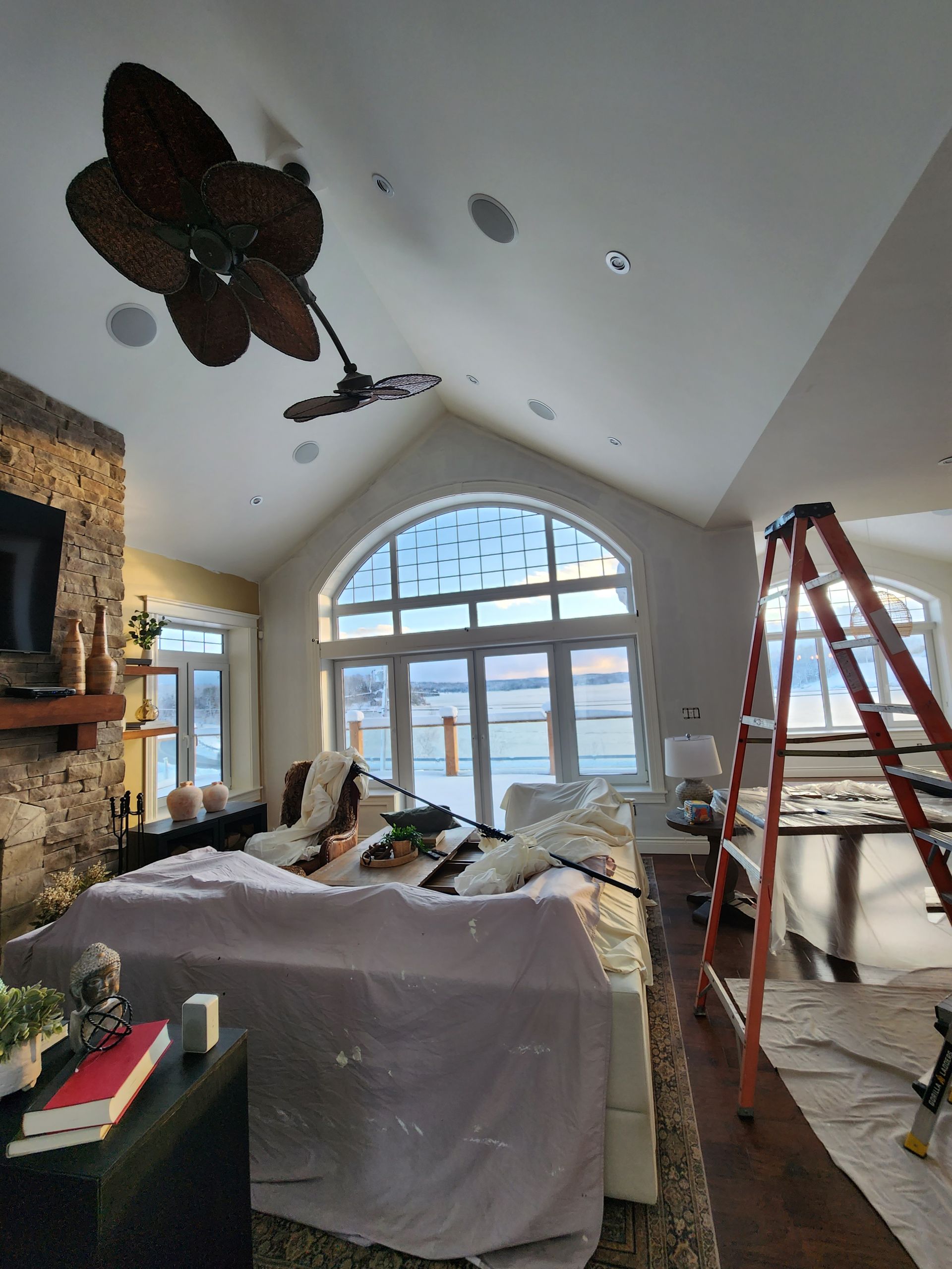 A living room with a ceiling fan and a ladder.