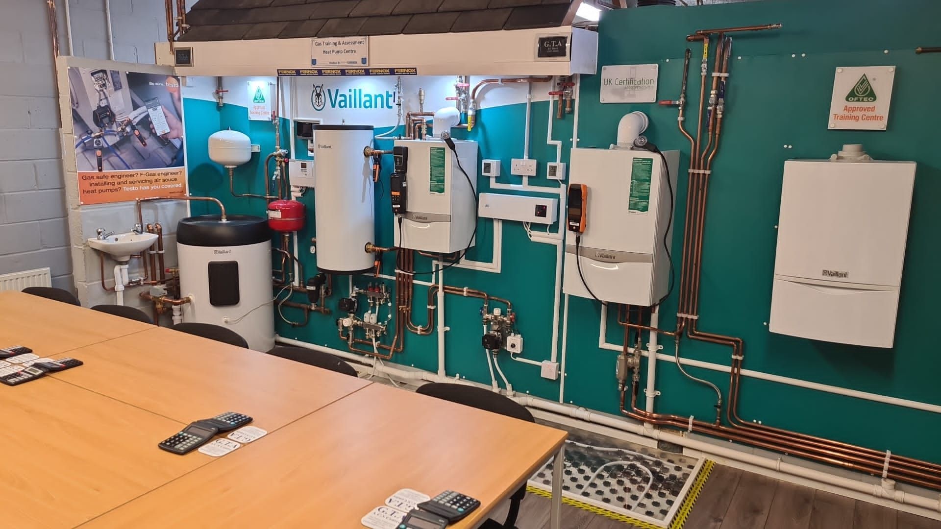 A room with a table and chairs and a wall with a bunch of boilers on it.