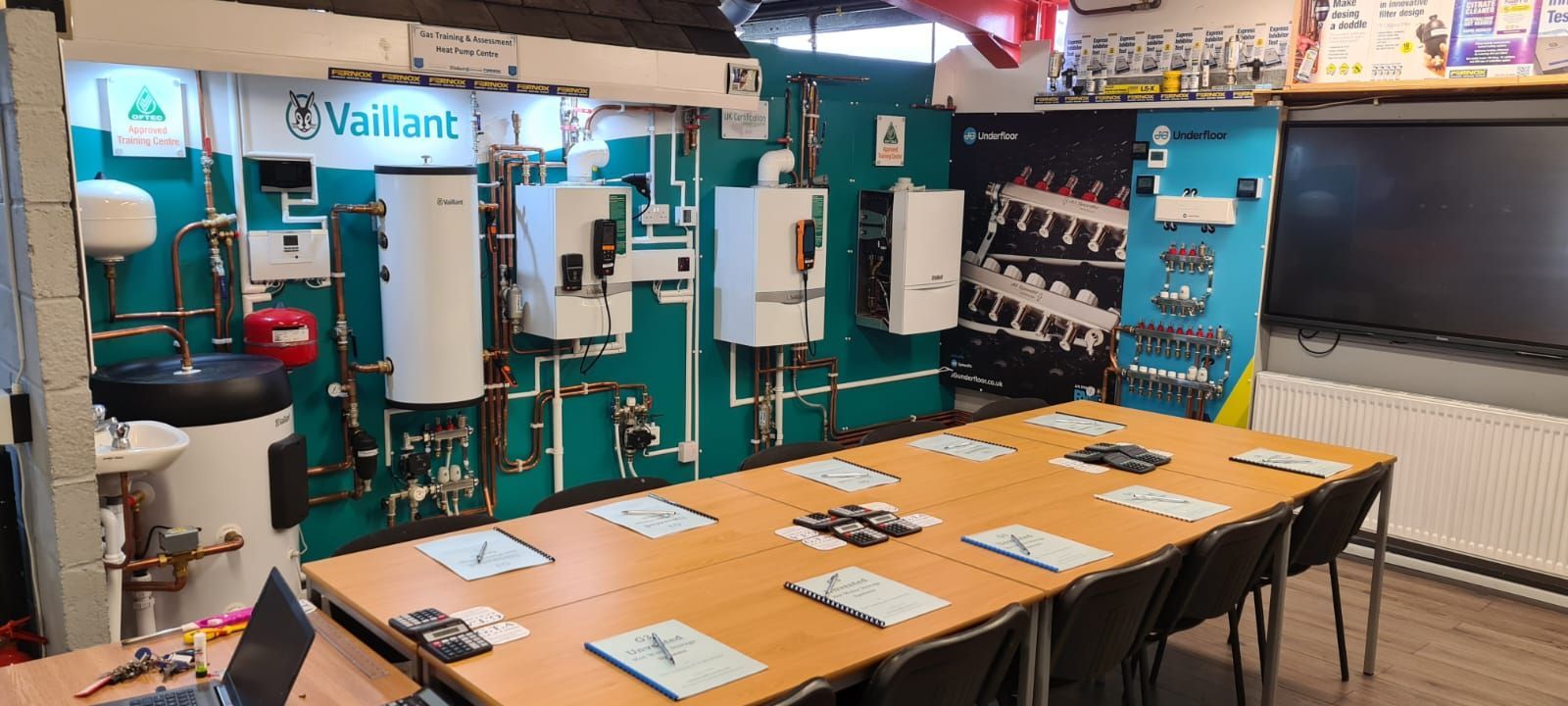 A conference room with a long table and chairs in front of a wall of boilers.
