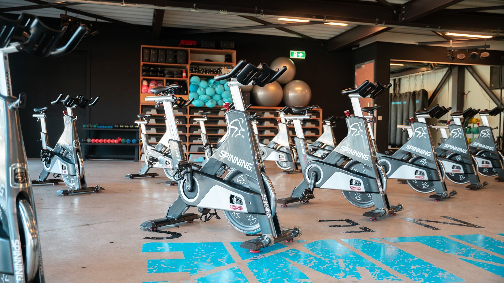 Gym studio with rows of stationary bikes, exercise balls, and workout equipment inside.