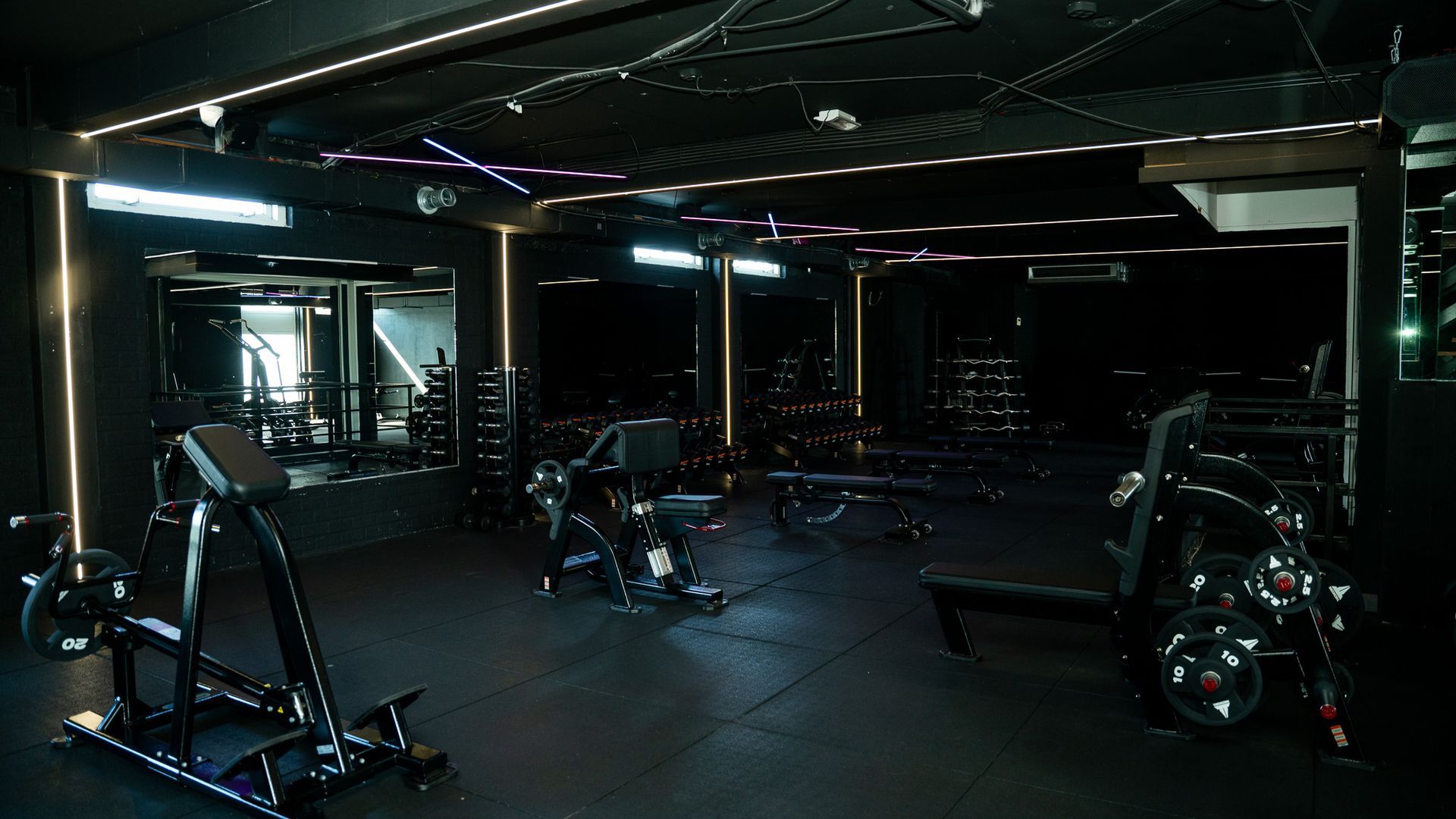 Dimly lit modern gym with weight machines and reflective mirrors, mostly empty.
