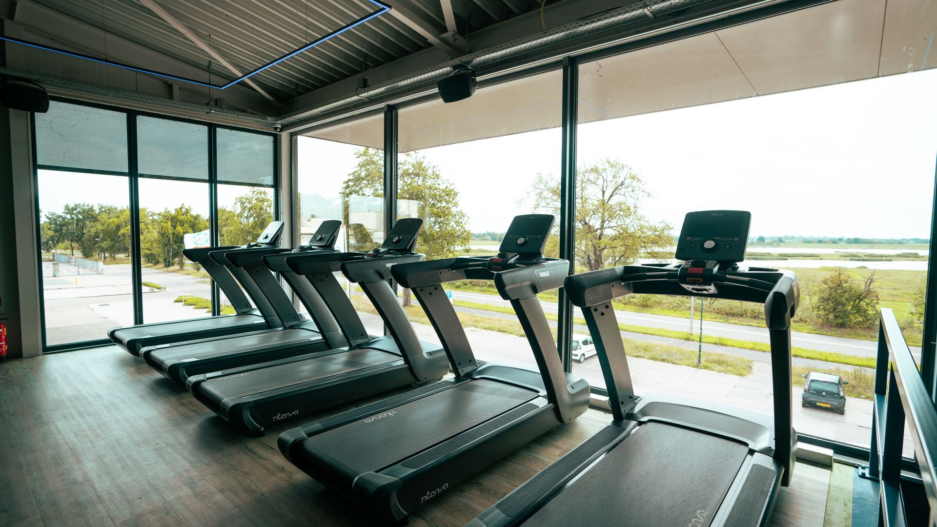 Modern gym with treadmills beside large windows overlooking water and trees