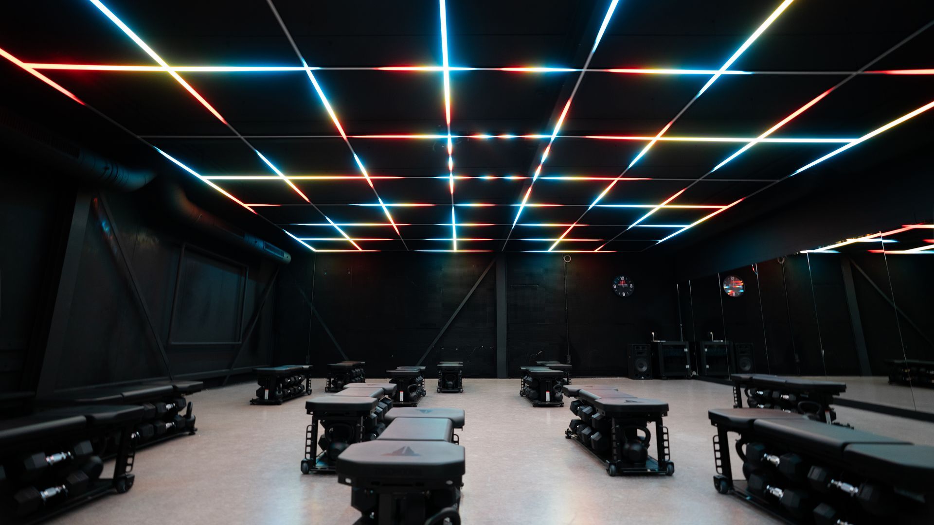 Empty futuristic room with long benches and tables under colorful neon grid ceiling lights