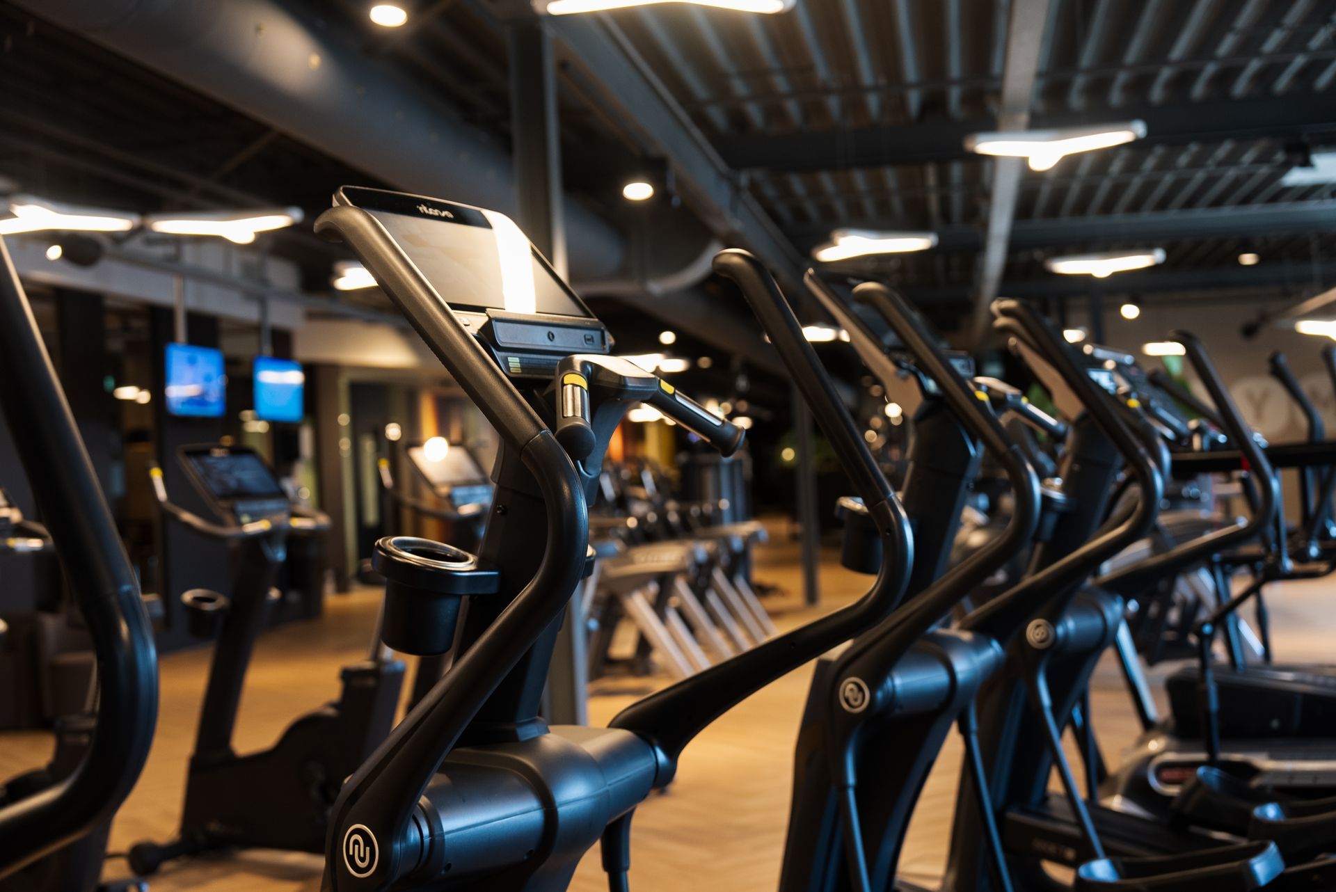 Row of stationary exercise bikes in a dimly lit gym with black frames and mirrors behind them