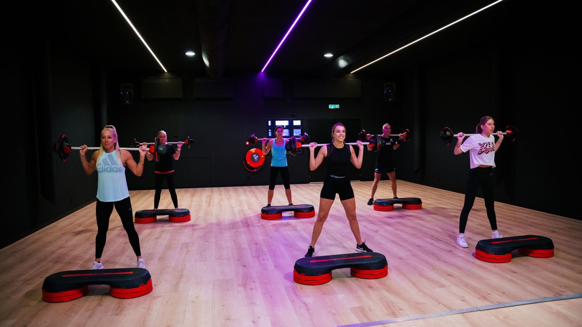 People exercising on step platforms in a dance fitness studio with bright neon lights