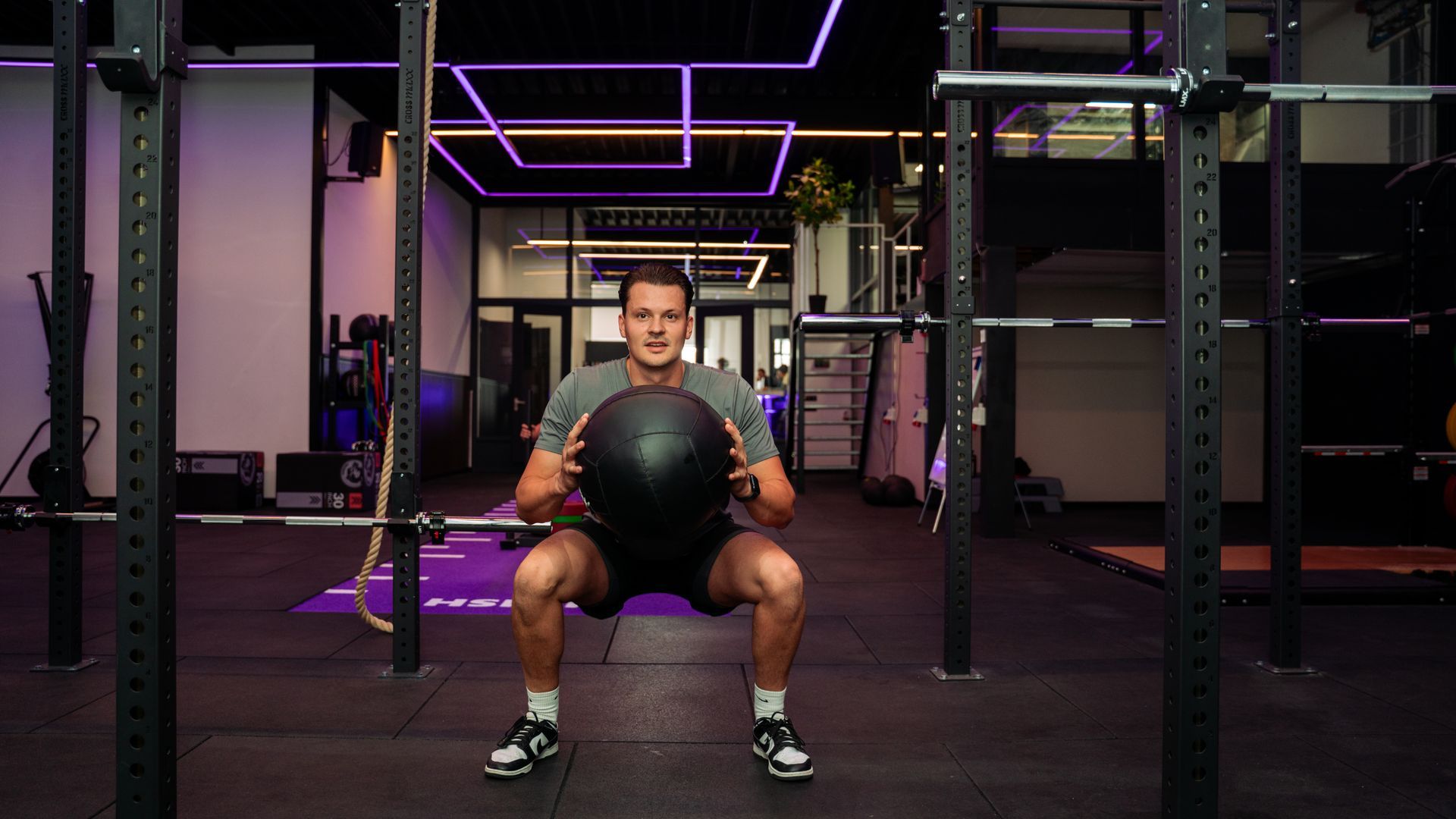 Person seated on a bench holding a medicine ball in a neon-lit gym