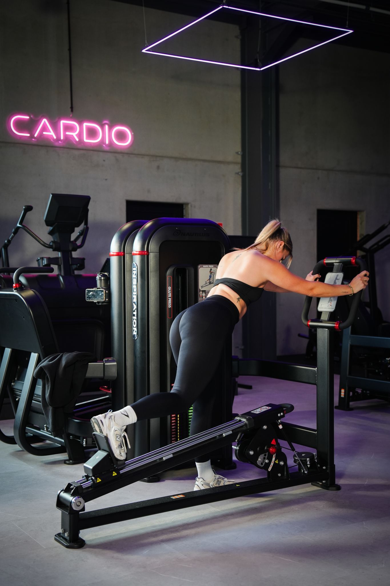 Vrouw die aan het sporten is op een fitnessapparaat in een cardiozaal met neonverlichting.