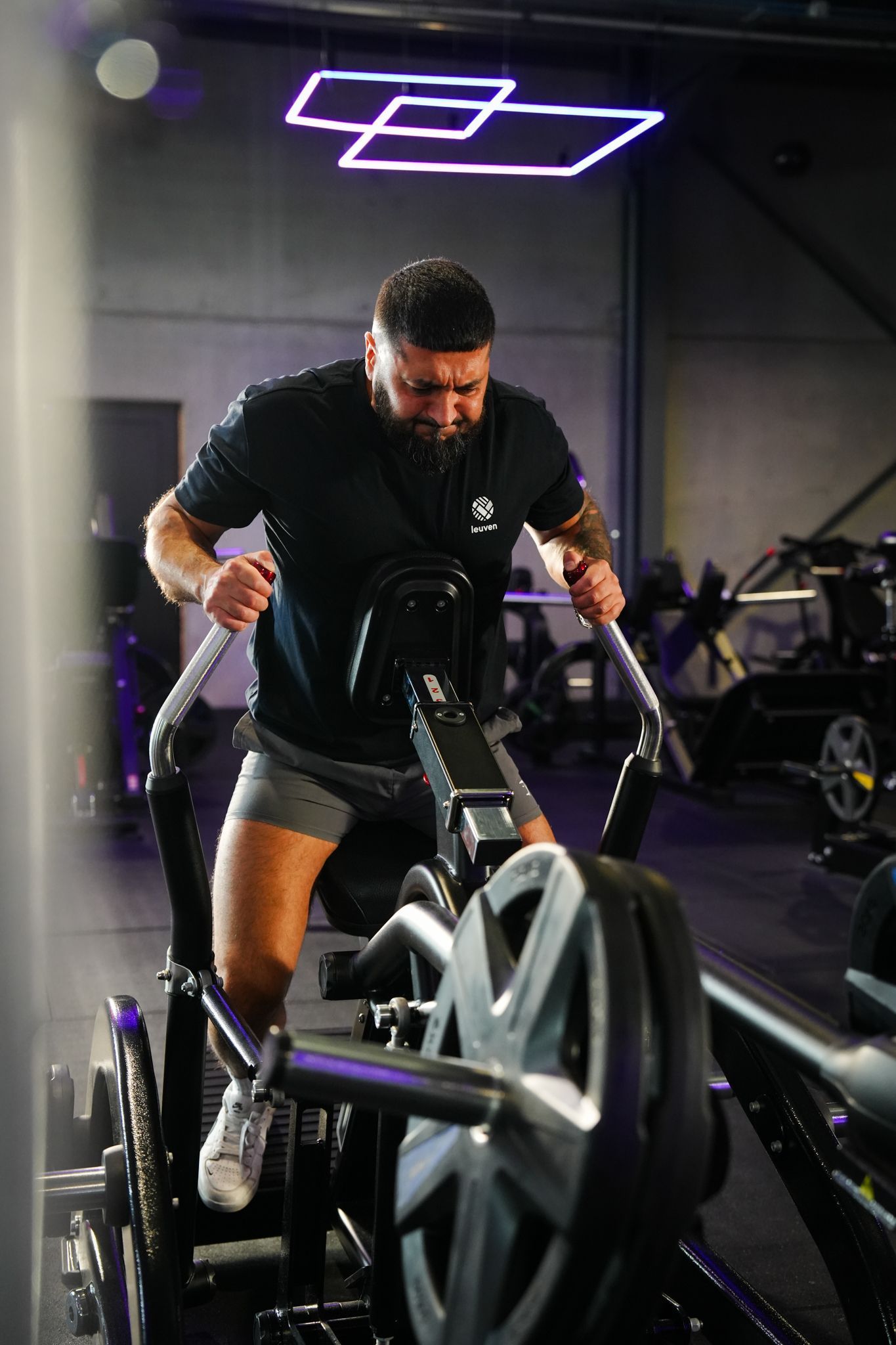 Een man traint op een ski-ergometer in een donkere sportschool met paarse neonverlichting.
