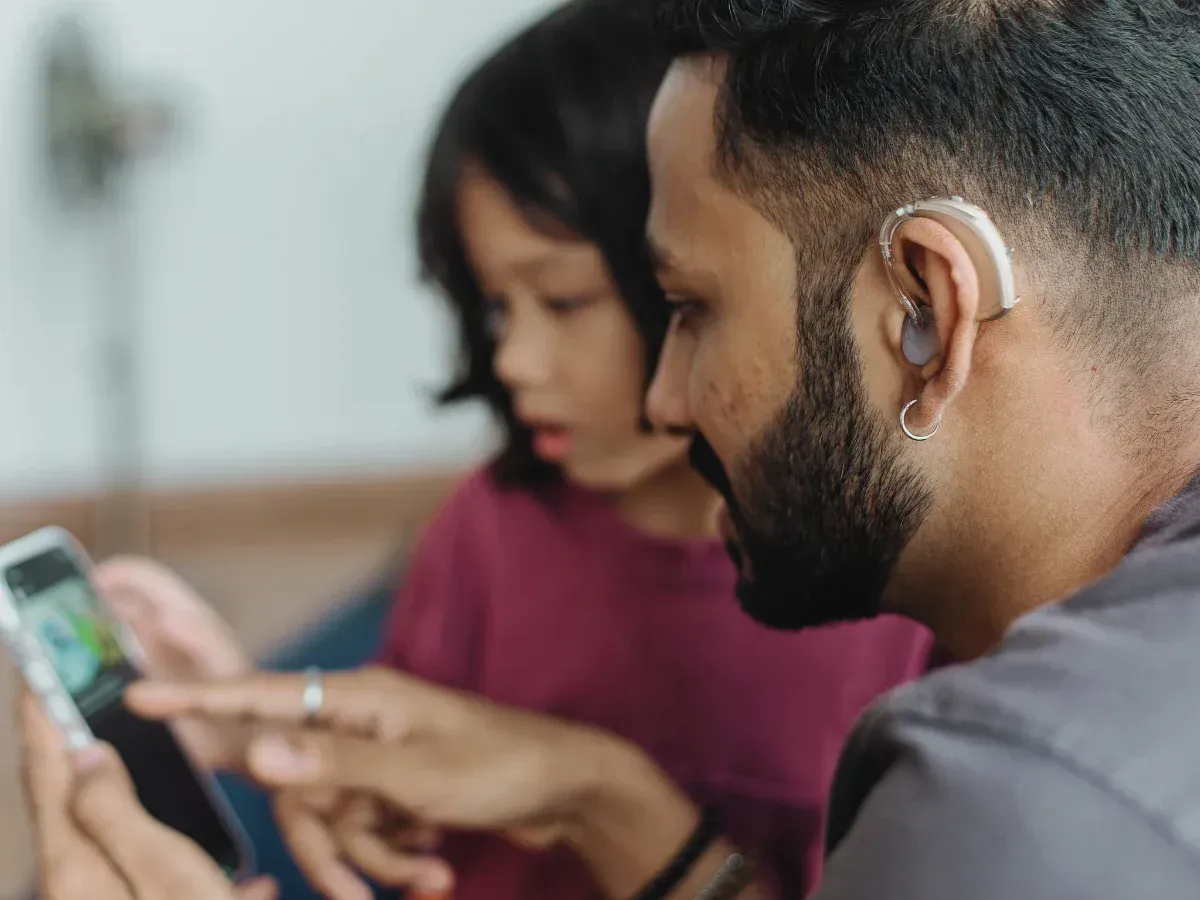 man with a hearing aid and child looking at smartphone