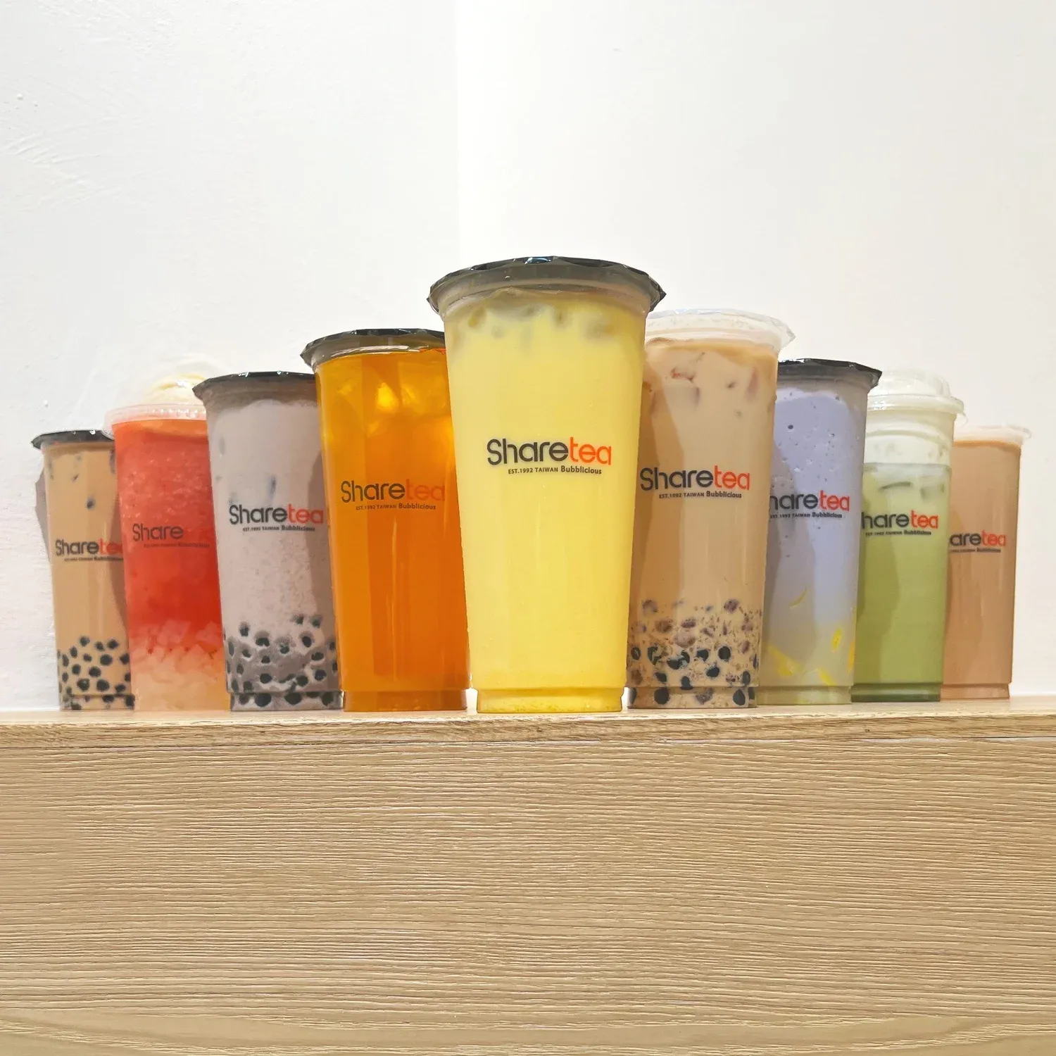 Assorted colorful bubble tea drinks lined up on a wooden shelf.