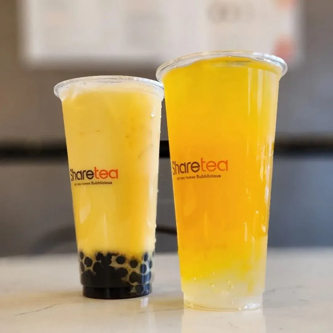 Two plastic cups of yellow bubble tea, one with tapioca pearls, on a counter