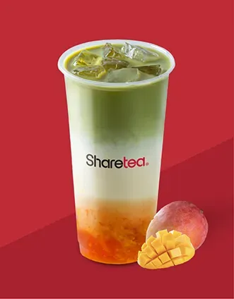 Mango iced tea in a clear cup with ice, green top and orange bottom, on a red background with mango slices