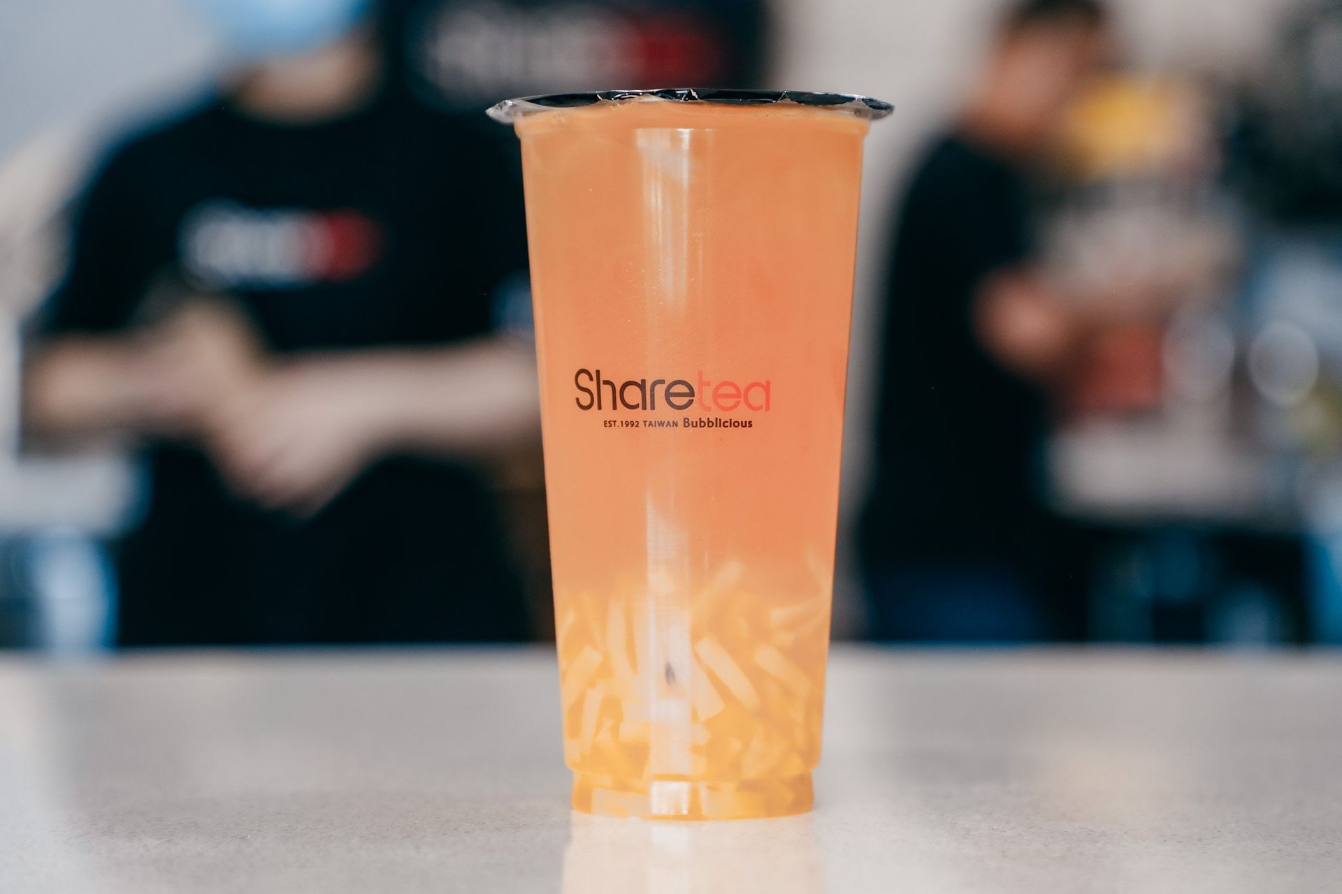 Orange smoothie cup with a clear lid on a table, blurred café background