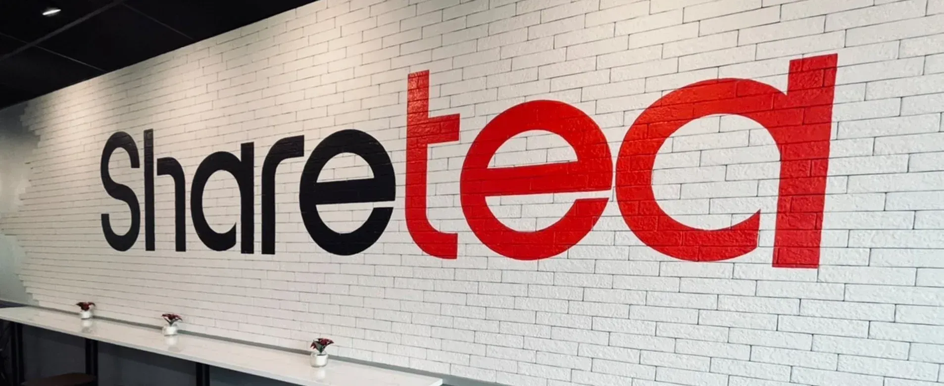 Sharetec logo on a white brick wall, with black “Share” and red “tec” lettering
