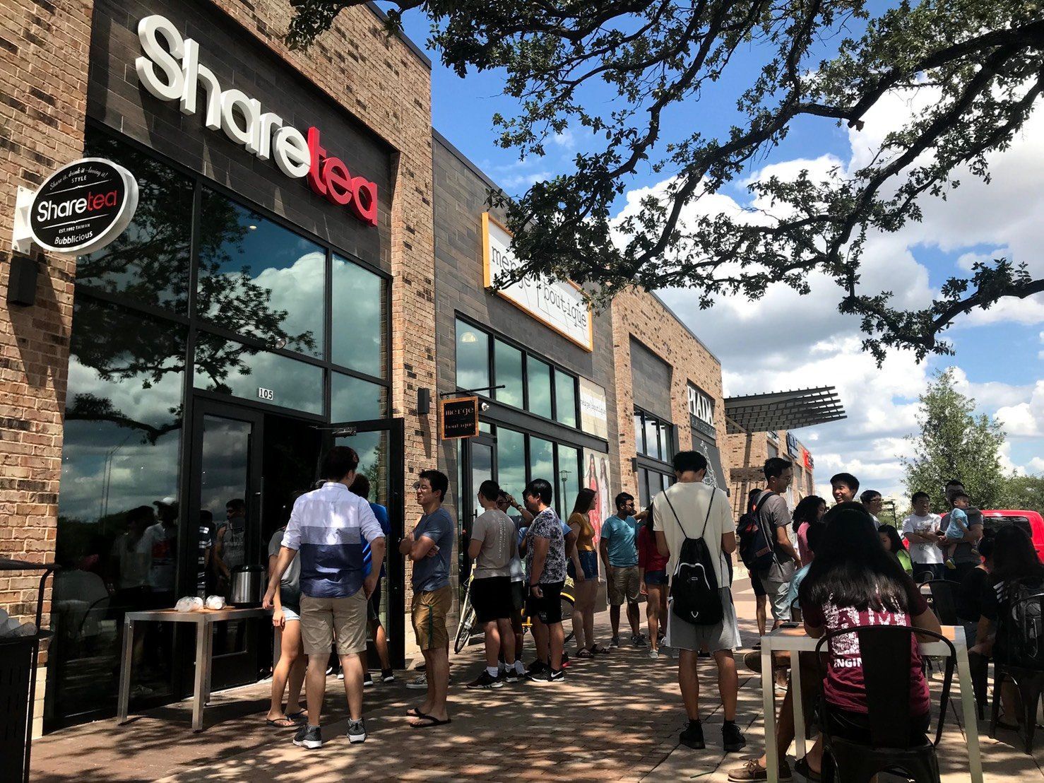 People waiting outside a Sharetea storefront on a sunny brick walkway