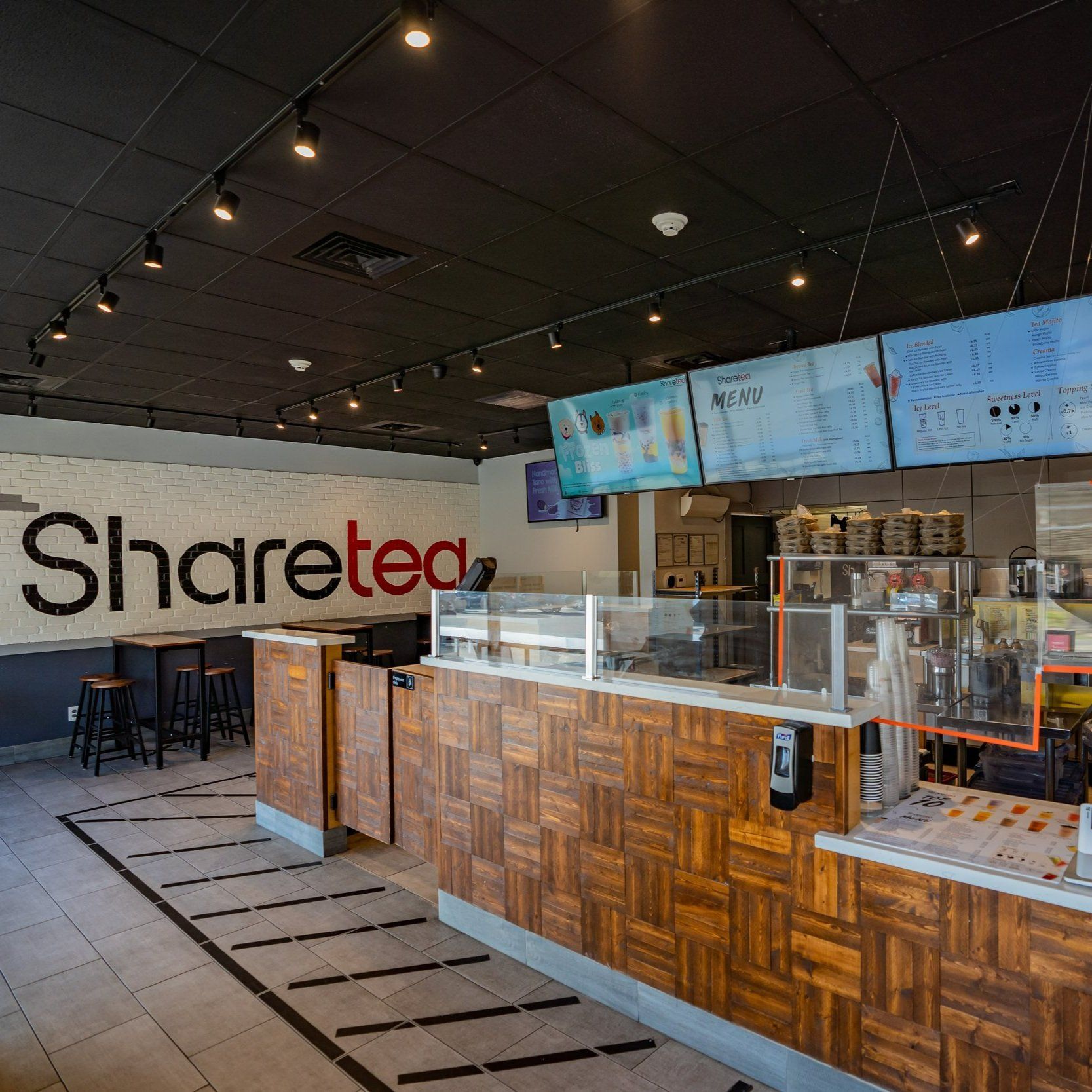 Sharetea café interior with wooden counter, menu screens, and black chairs under string lights