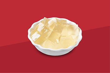 White bowl of translucent yellow jelly cubes on a red background