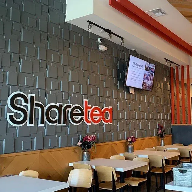 Sharetea café interior with wall sign, tables, chairs, and a menu screen on a geometric gray wall
