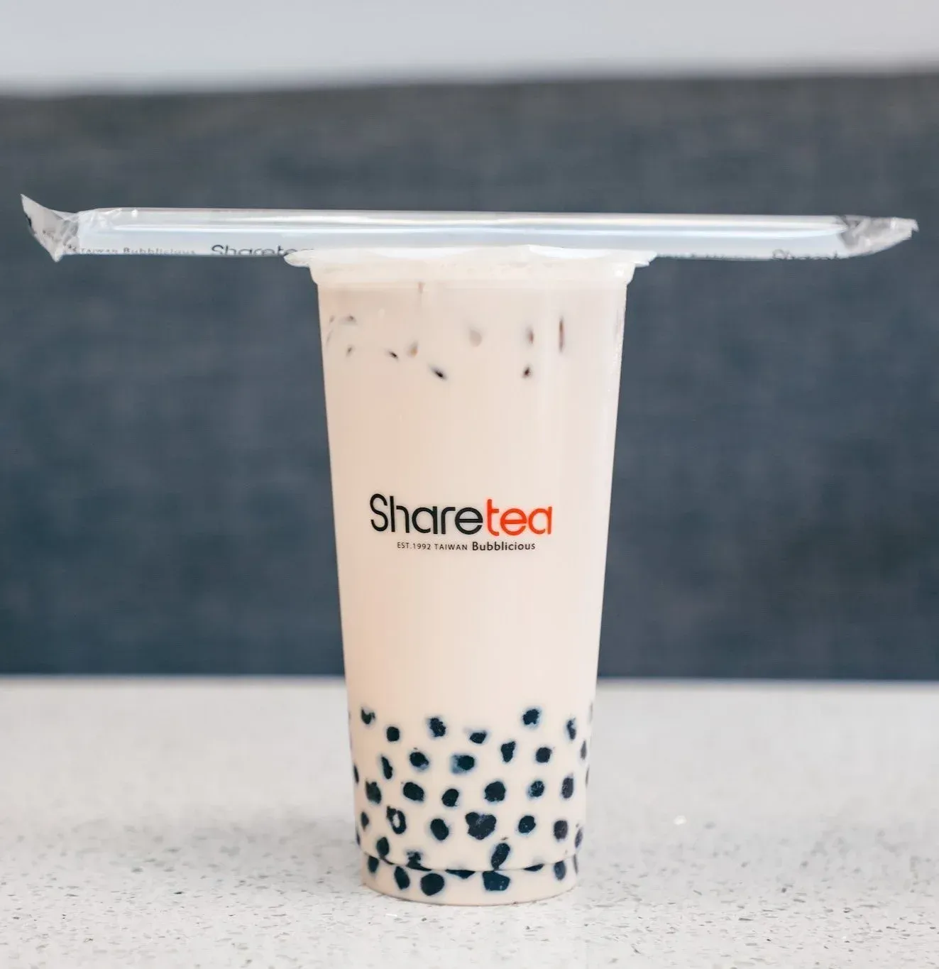 A plastic cup of milk tea with black tapioca pearls and a sealed lid on a white table