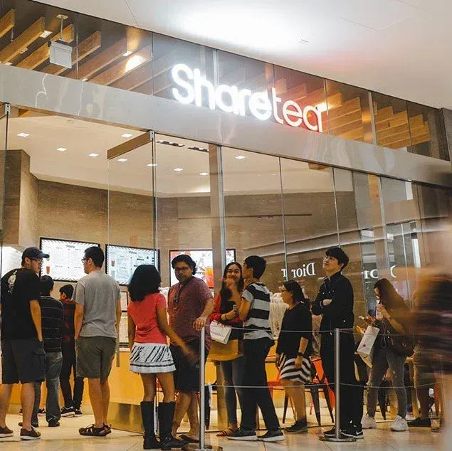 People standing outside a ShareTea shop with glass doors and bright interior lighting