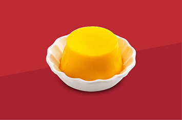 Yellow pudding dessert in a white shell-shaped dish on a red background