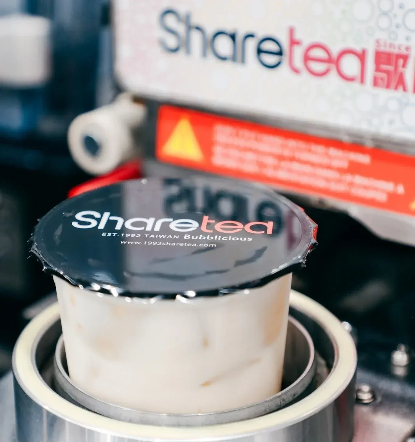 Sealed Sharetea drink cup in a beverage machine, with Sharetea sign blurred in the background