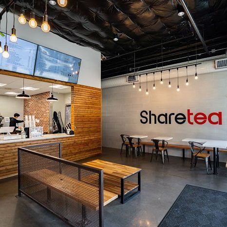 Modern tea shop interior with wooden benches, hanging lights, and “Sharetea” sign on the wall