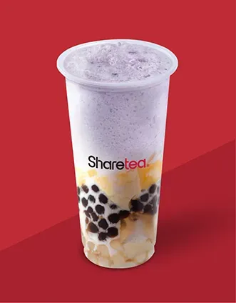 Tall bubble tea with purple foam and black tapioca pearls in a clear cup on a red background
