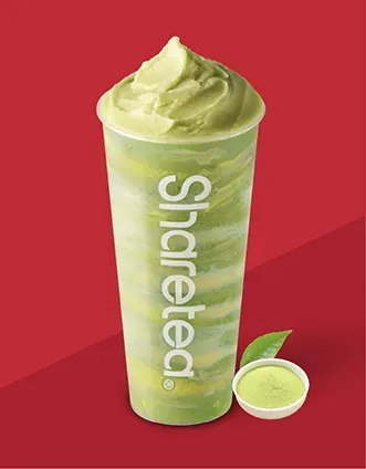 Green Sharetea drink in a clear cup with a whipped top on a red background, with a small sample cup beside it