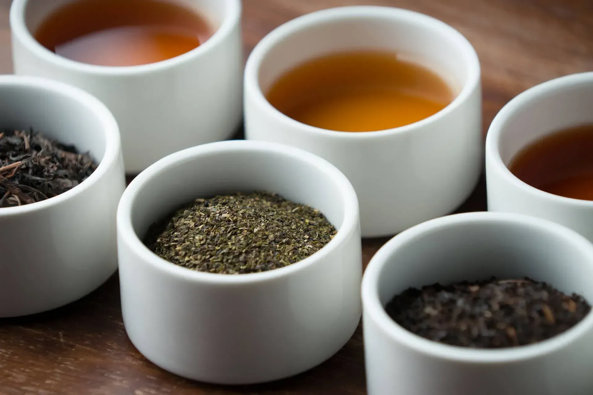 Assorted loose leaf teas in white cups on a dark wooden table