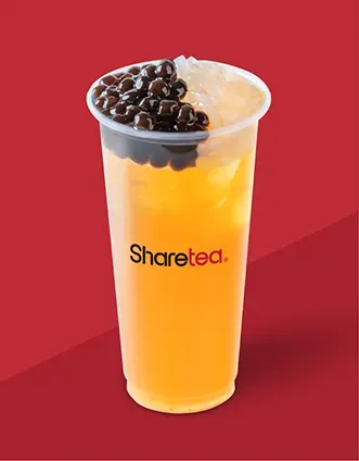 Clear plastic cup of orange iced drink topped with dark boba pearls on a red background