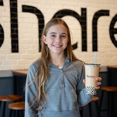 Smiling person holding a bubble tea drink in a cafe with a large wall sign behind them