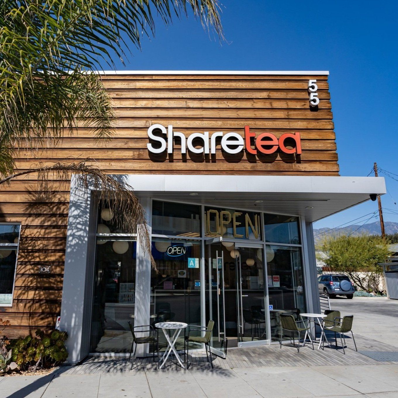 Storefront of Sharetea with wooden facade, glass entrance, and outdoor seating on a sunny street