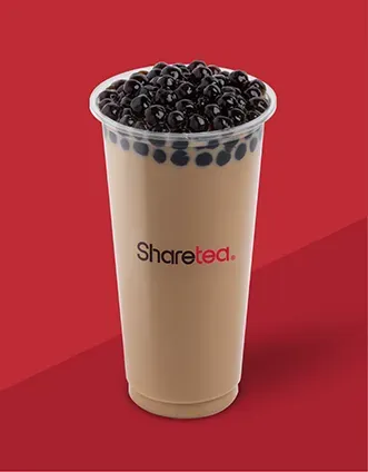 Tall tan milk tea topped with black tapioca pearls in a clear cup on a red background