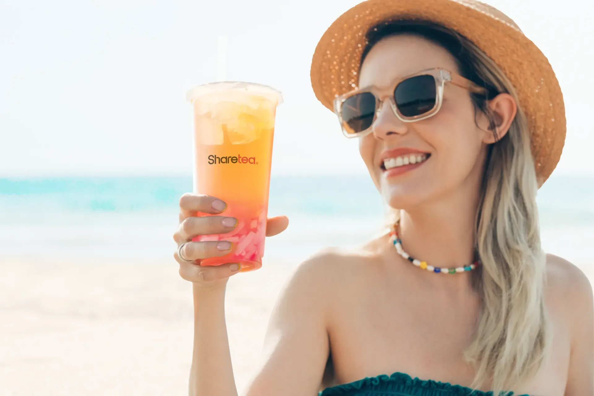 Woman in straw hat and sunglasses holding a colorful drink on a sunny beach
