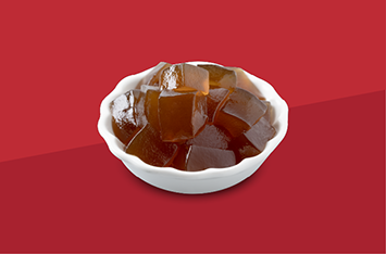 White bowl of brown gelatin cubes on a red background